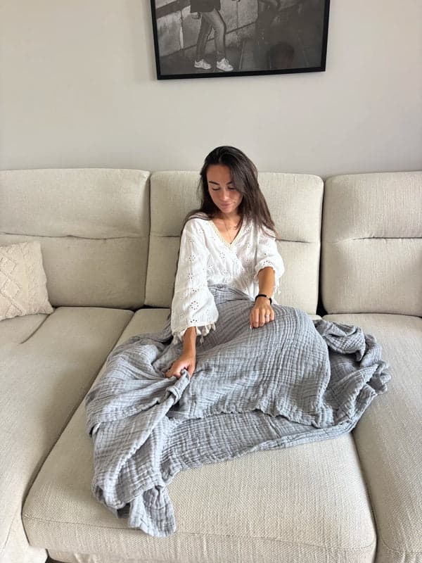 A person sitting on a pale sofa with a grey muslin blanket over their legs