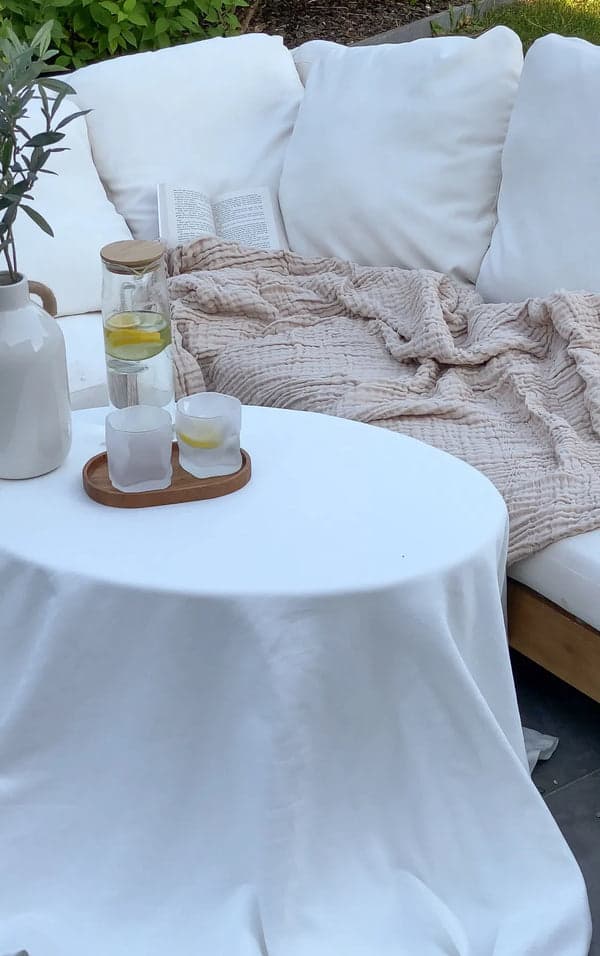 A beige muslin blanket on a garden sofa beside a small table