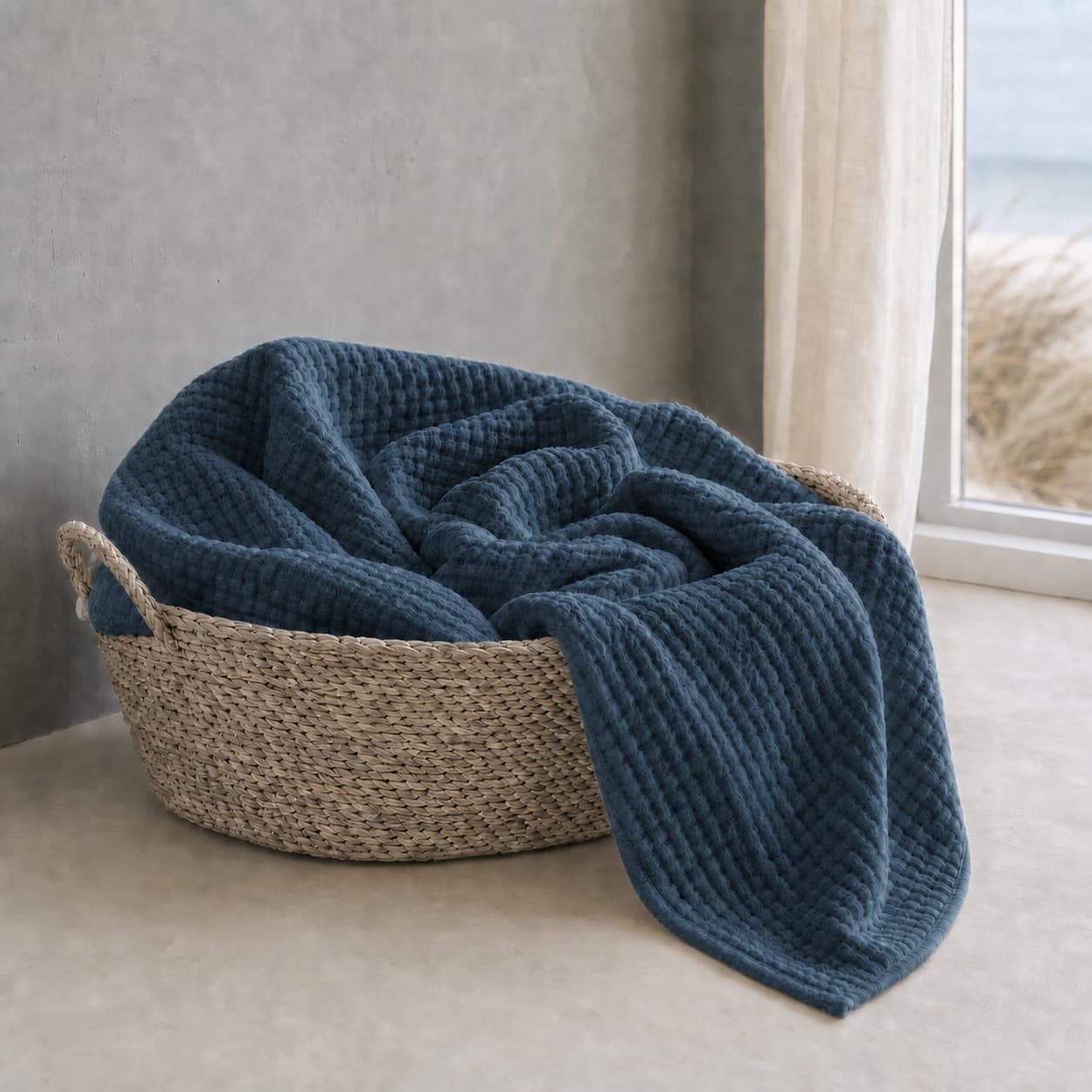 Lightweight deep navy muslin blanket in a basket by a window