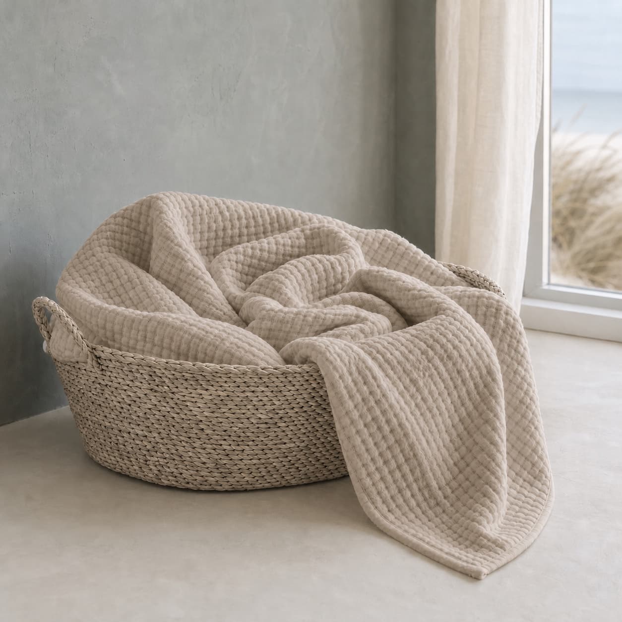 Lightweight warm beige muslin blanket in a basket by a window