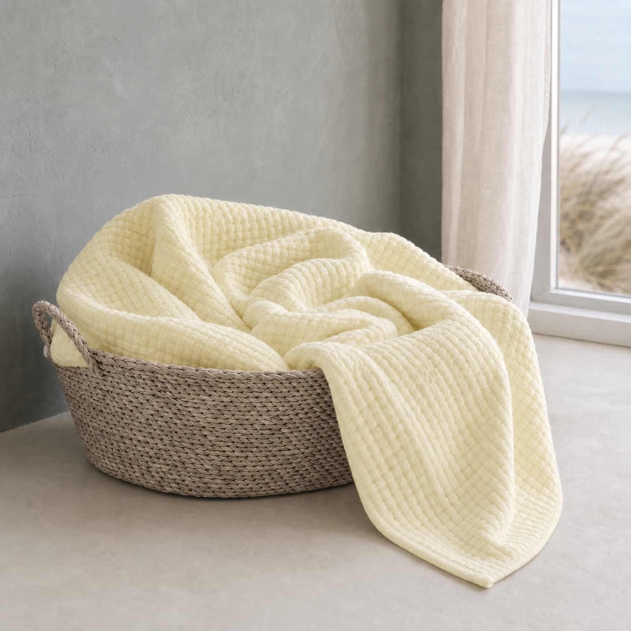 Cream-yellow lightweight muslin blanket in a basket by a window