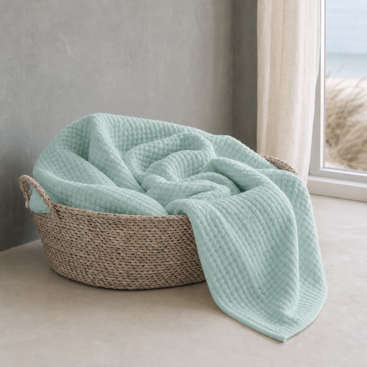 Lightweight mint green muslin blanket in a basket by a window