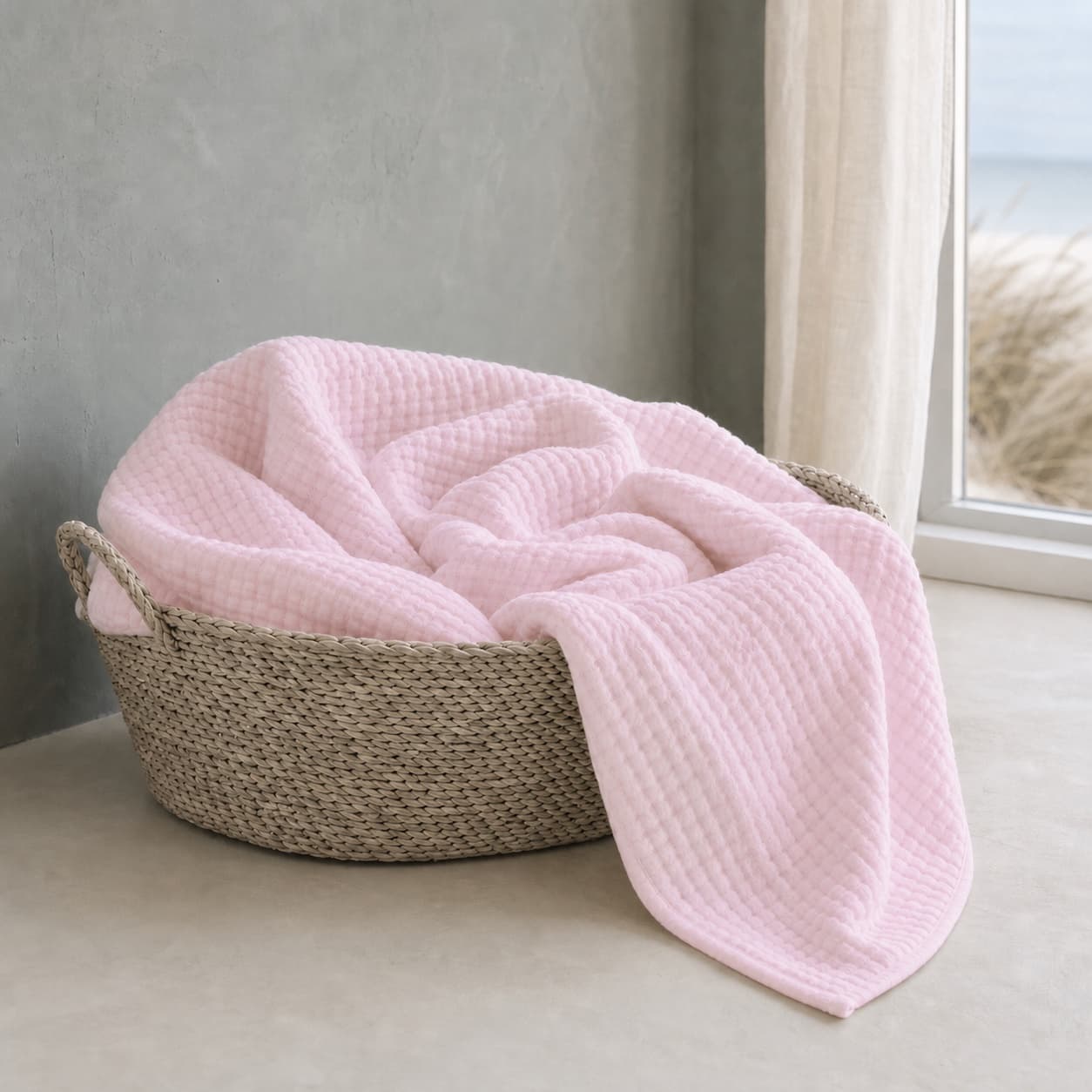Lightweight pale pink muslin blanket in a basket by a window