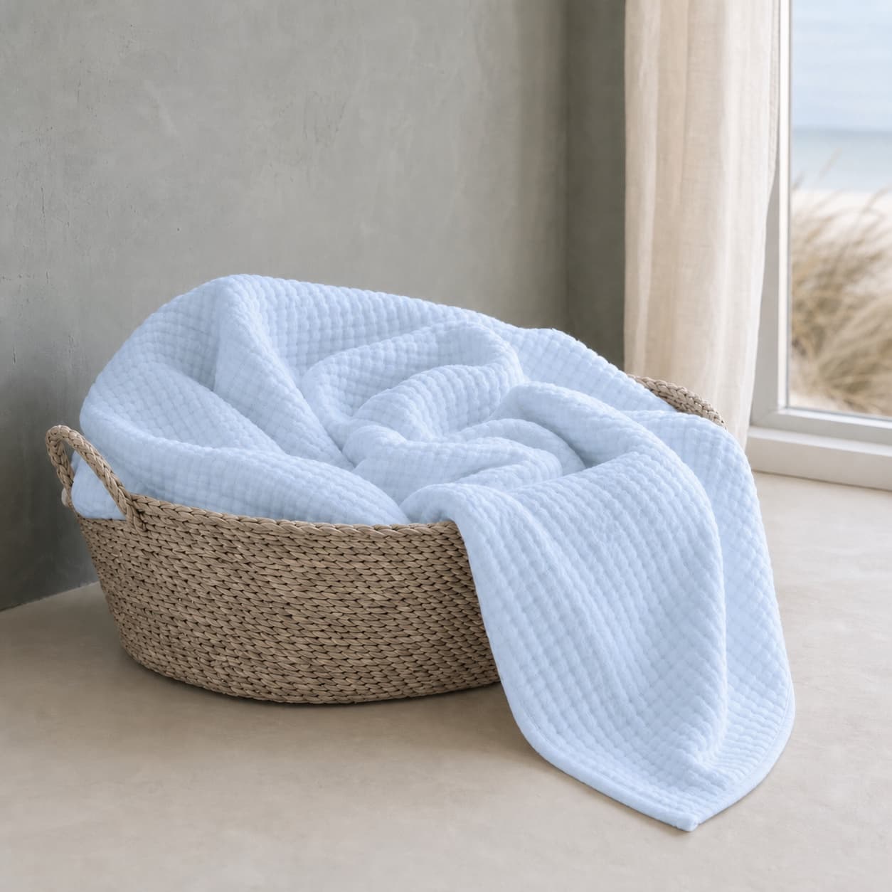 Lightweight sky blue muslin blanket in a basket by a window