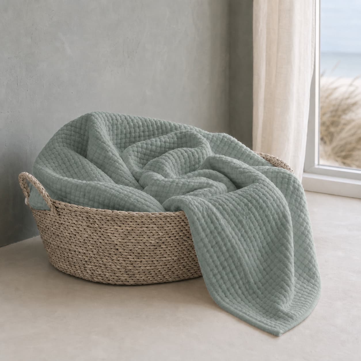 Sage green lightweight muslin blanket in a basket by a window